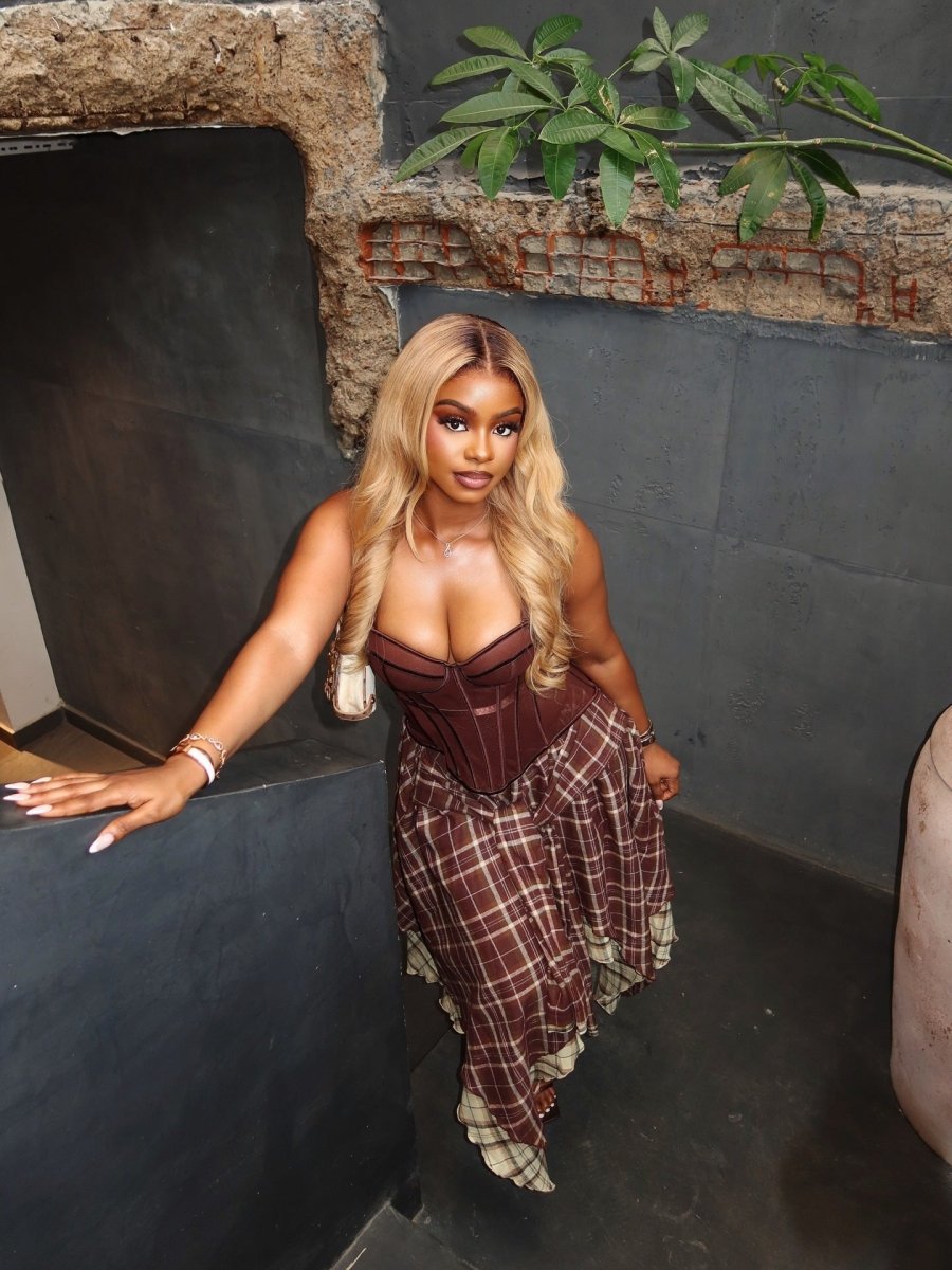Boned corset top and asymmetric plaid skirt co-ord set in brown and beige, worn by model from side, leaning against dark