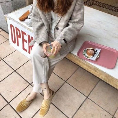 Model seated on a bench in the beige blazer with cream trousers and yellow mules