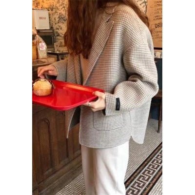 Boxy beige blazer worn open, model carrying a red tray with a bun