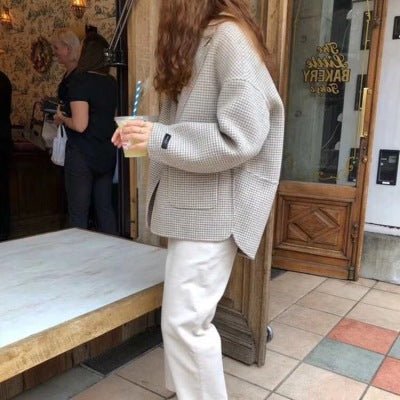Woman in a beige houndstooth blazer and cream trousers holding an iced drink outside a bakery