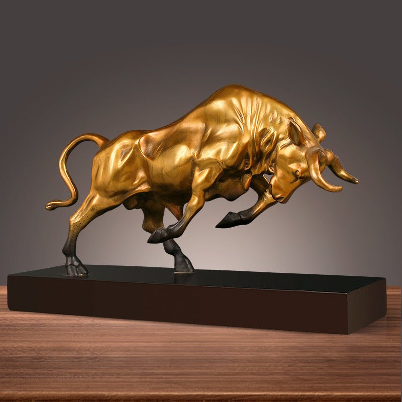Charging bull metal sculpture in gold finish on black base, side view, freestanding on wooden surface
