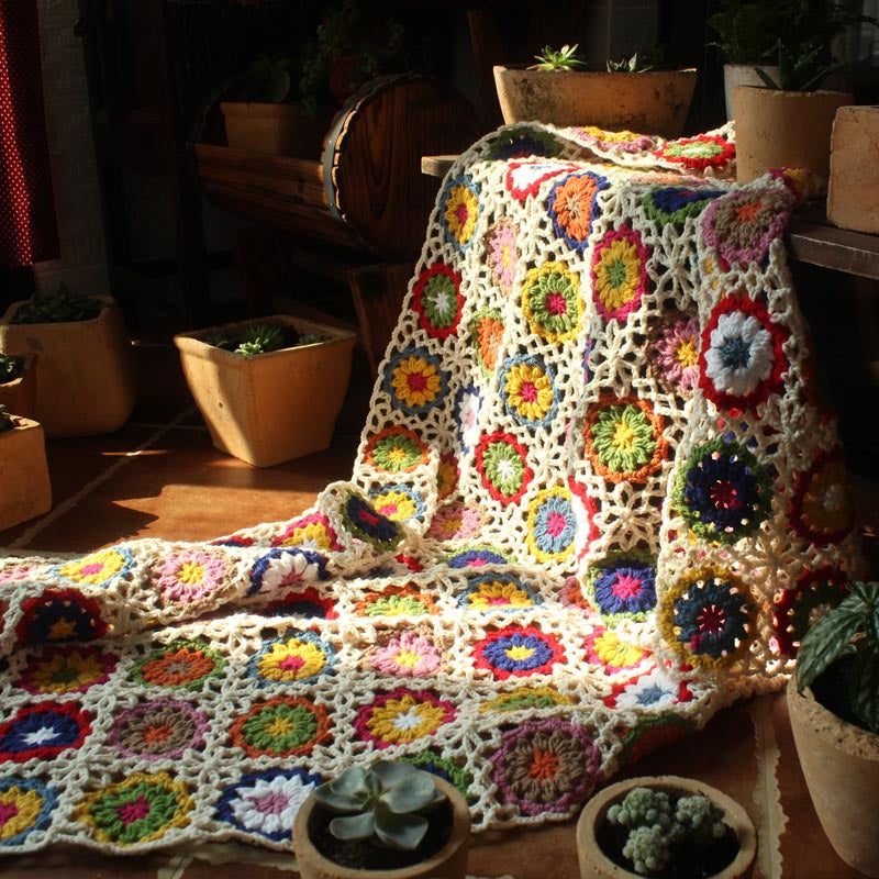 Crochet flower throw, multicolour, draped on floor in sunlit room with potted plants