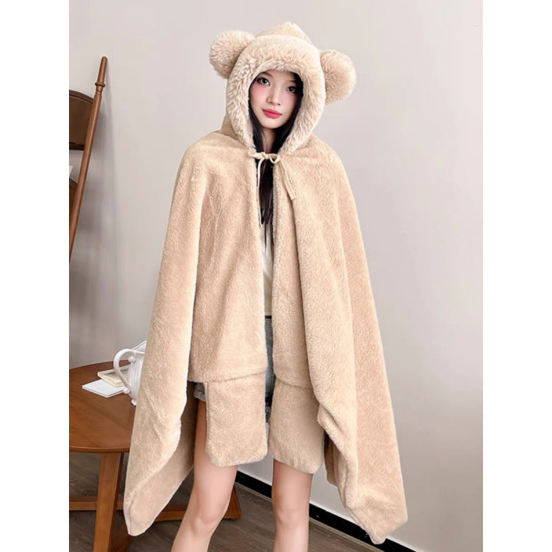 Beige hooded fleece nap cape with bear-ear hood, worn by a model, full front view, standing indoors near wooden table