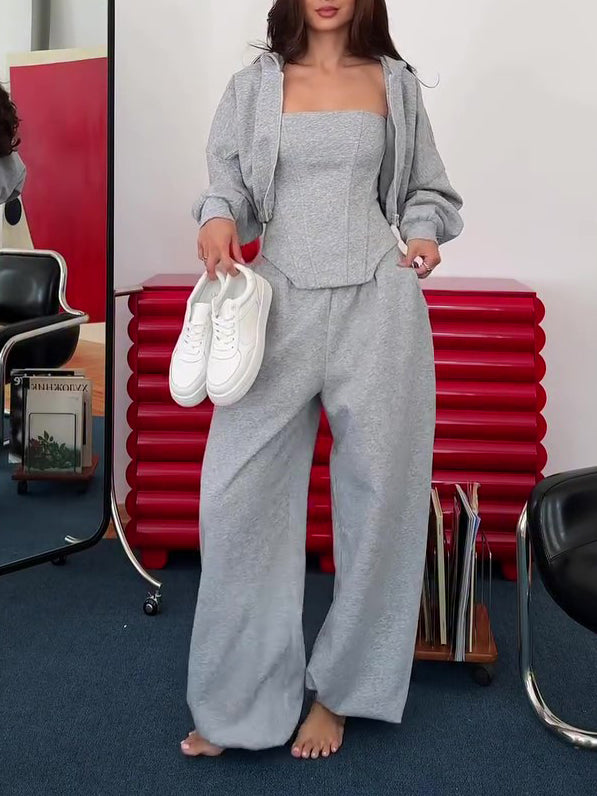 Grey corset top, cropped hoodie and wide-leg trousers set on model, front view, holding white sneakers, barefoot