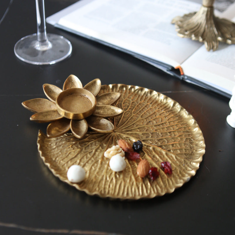 Brass lily pad tray with lotus tealight holder, flat lay, gold colour, holding nuts and berries, on dark table with book and