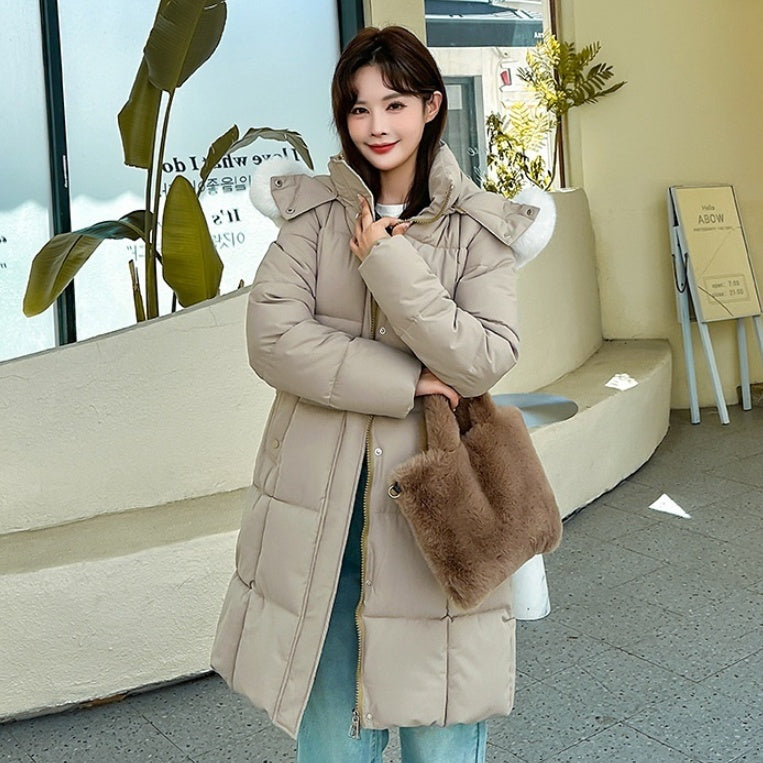 Mid-length padded coat in beige with faux-fur hood, worn by a model outdoors, front view, carrying a brown fur bag