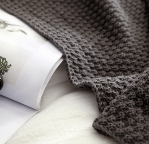 Dark grey chunky knit throw draped over a book on a white bedspread