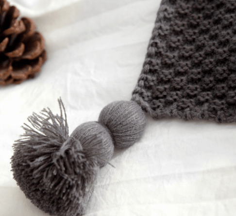 Detail of dark grey chunky knit throw with three-tiered pompom tassel on white background