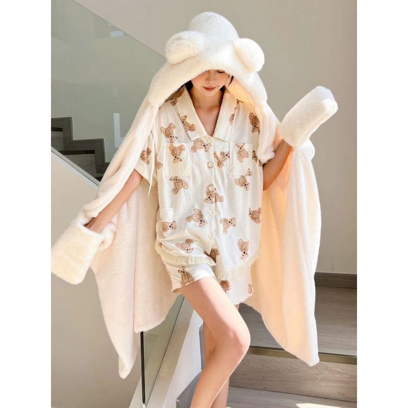 White hooded fleece nap cape with bear-ear hood, worn by a model over pajamas, standing on staircase, front view