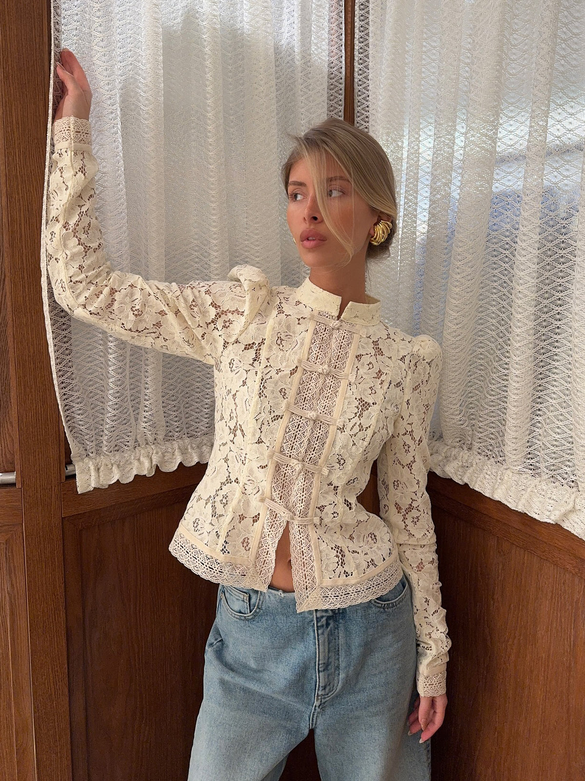 Front view of lace-panel blouse with puffed shoulders, cream floral lace, stand collar, on model standing near window