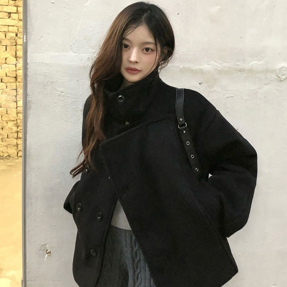 Black cropped wrap jacket on model, angled front view against light wall, bag strap over shoulder, hands in pockets