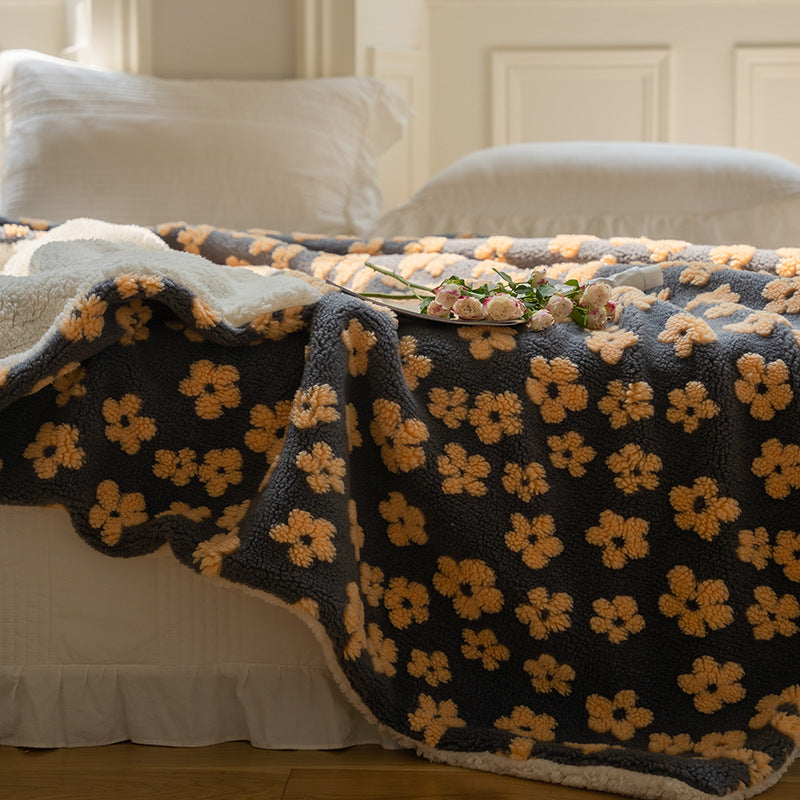 Floral jacquard sherpa-back throw blanket in navy with beige flowers, spread over a bed, with a tray of flowers on top