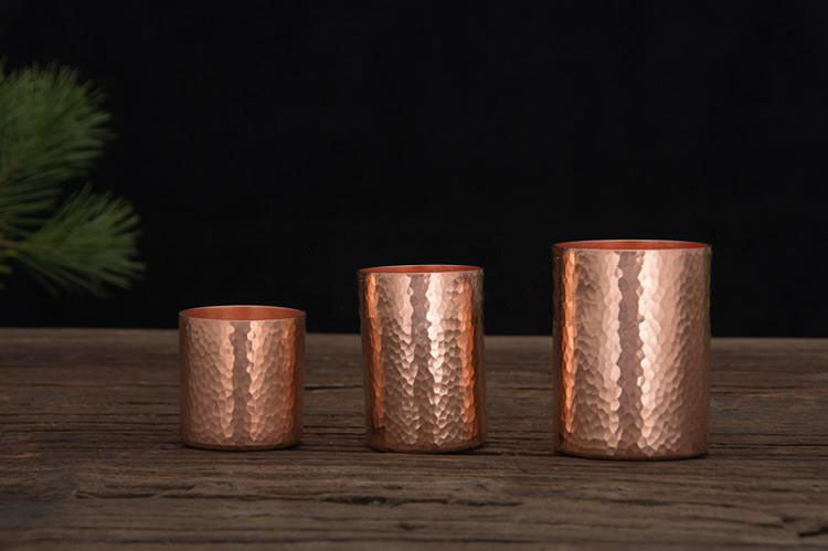 Three hammered metal tea cups, copper colour, aligned in a row on wooden surface