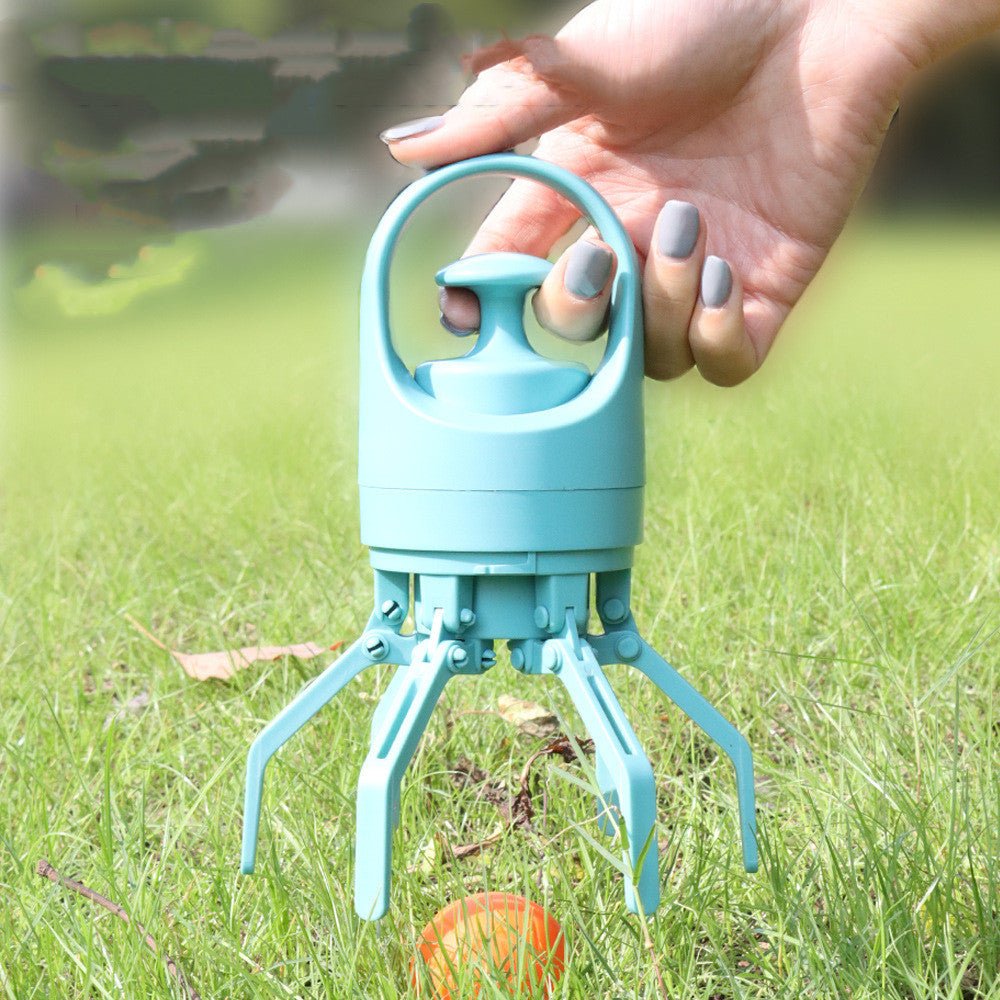 Hand pressing the button of a teal dog poop picker on grass, claws open over an orange ball