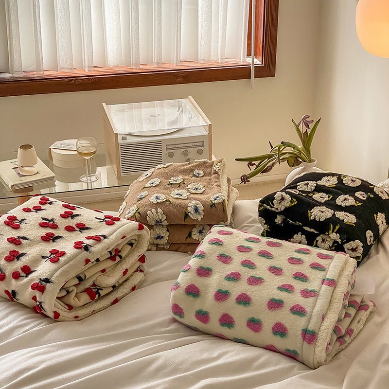 Folded blankets with cherries, brown daisies, black daisies and pink strawberries on a bed