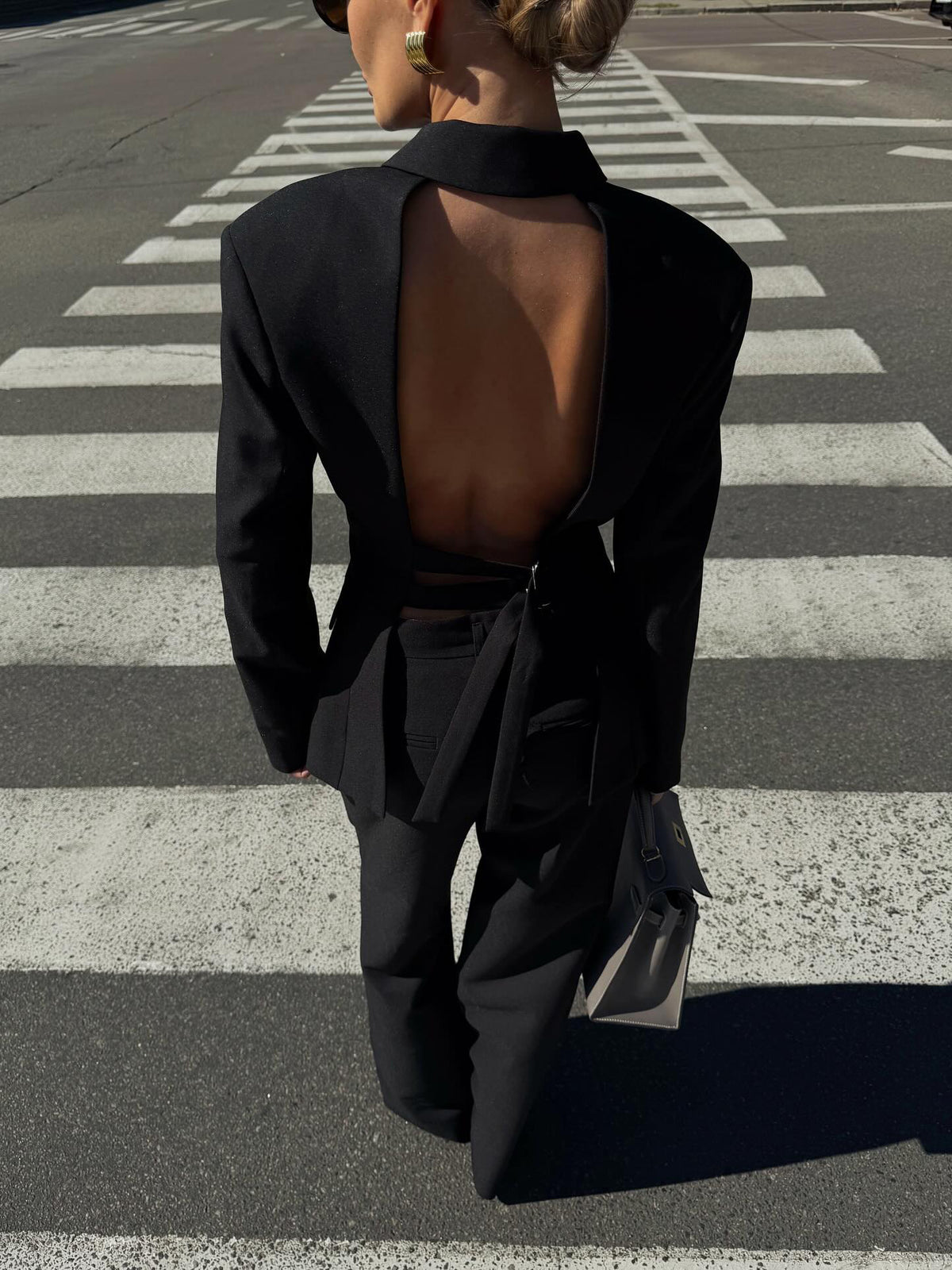 Back view of the black open-back blazer and wide-leg trouser suit on a model walking across a zebra crossing