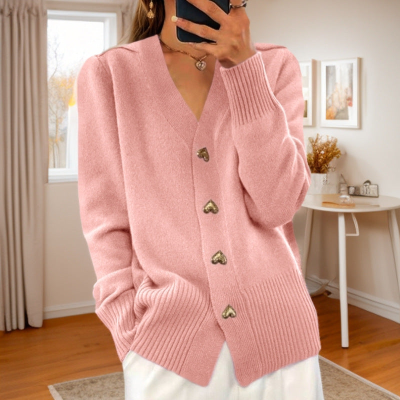 V-neck knit cardigan in pink with heart-shaped buttons, worn by a model in a cozy room