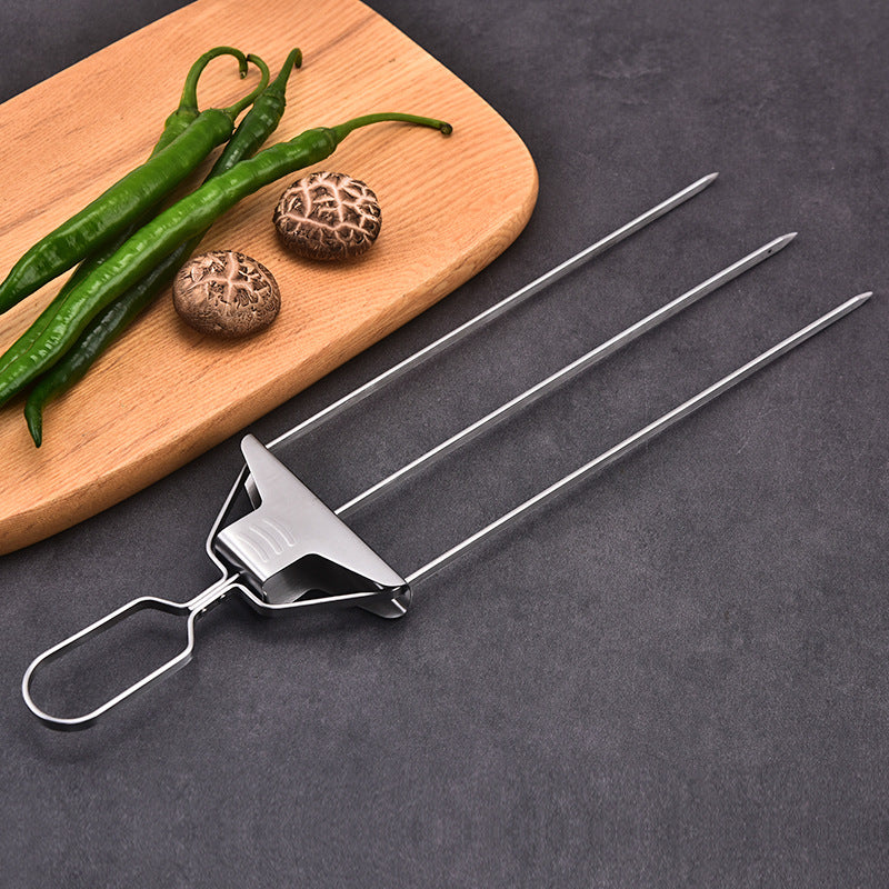 Three-prong stainless steel skewer with slide-off pusher and loop handle, placed next to green peppers and mushrooms on a