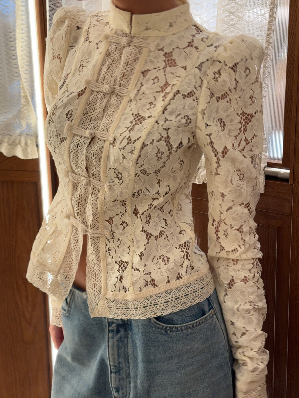 Close-up of cream floral lace blouse with puffed shoulders and front toggle closure, worn by model