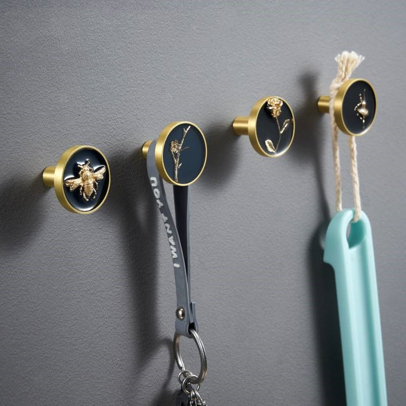 Enamelled drawer knobs with gold-tone rim in use on a wall, featuring blue bee, blue wintersweet, black rose, and black
