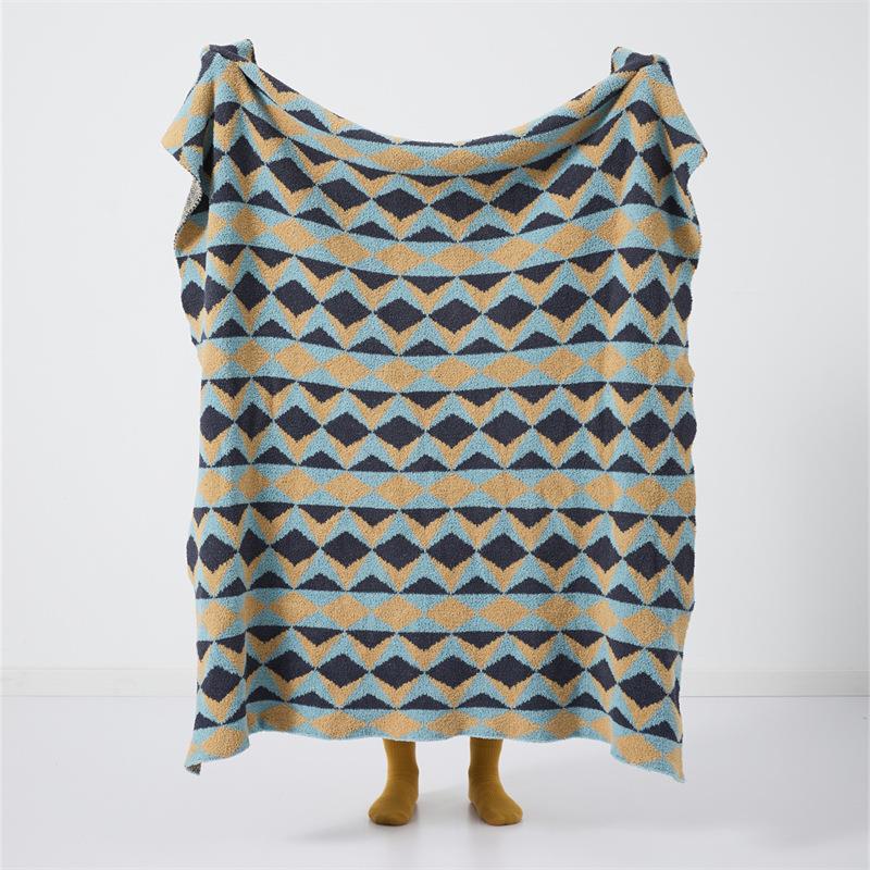 Geometric diamond-pattern knit throw in blue, mustard and charcoal, displayed flat on mannequin legs against white background