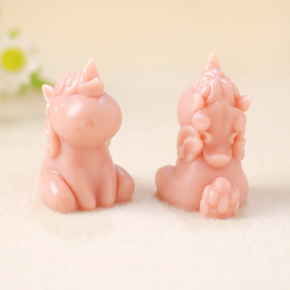 Two pink unicorn-shaped candles, one facing forward and one backward, on light fabric surface with green flowers in