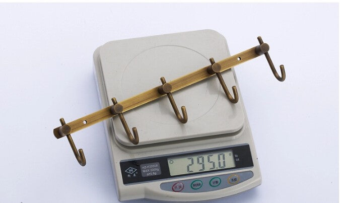 5-hook wall rail in antique brass-tone finish, placed on digital scale showing weight of 295.0 g