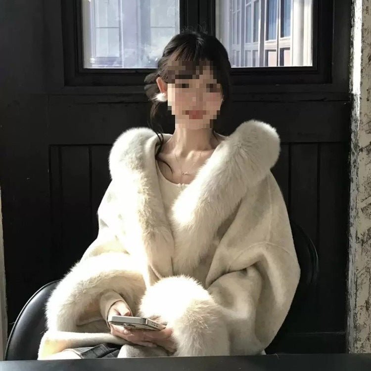 Seated model in the cream wrap coat, fur trim framing the neckline