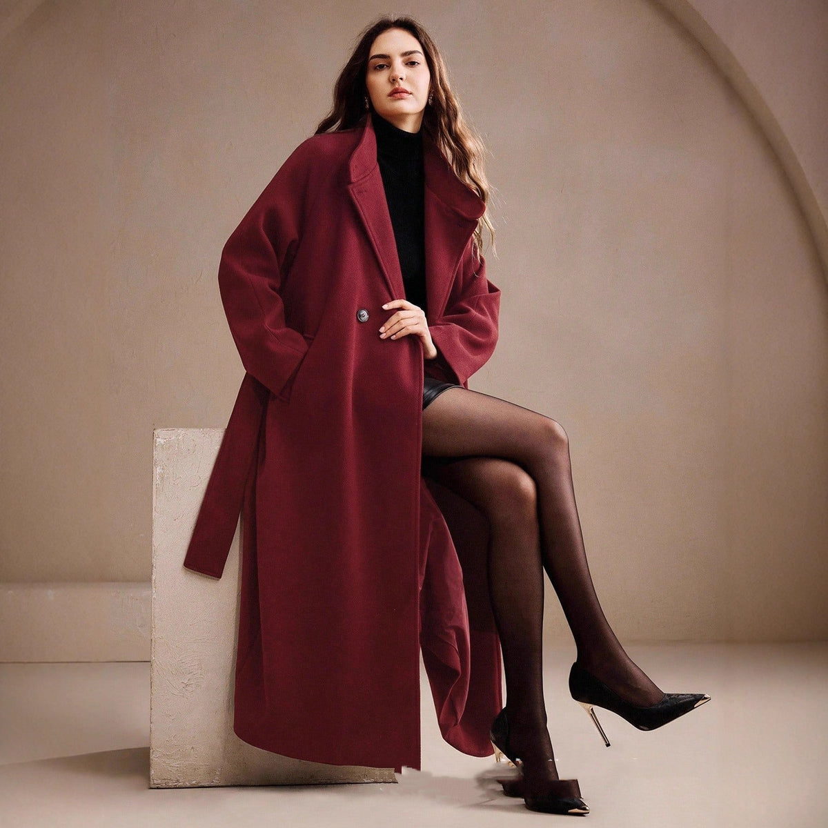 Long double-breasted wrap coat in wine red, wide lapel, worn by model seated on block, front view