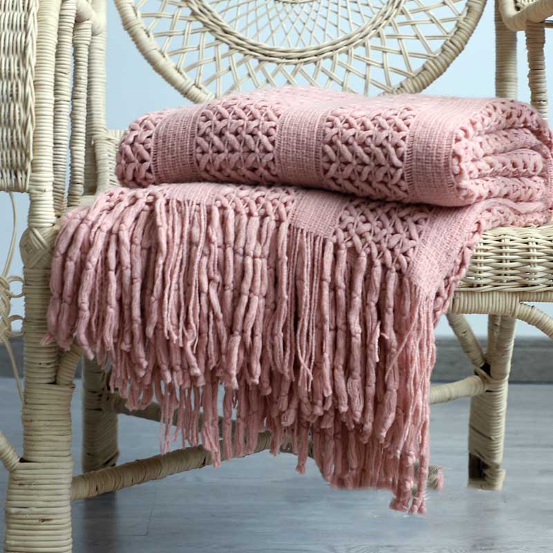 Chunky lattice knit throw in pink with tassels, folded on a wicker chair, front view