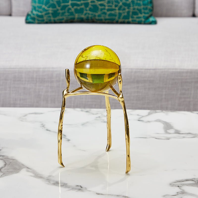 Amber glass ball on the tall gold-tone stand on a white marble table