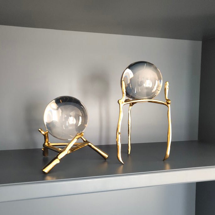 Two clear glass balls on a low and a tall gold-tone stand on a grey shelf