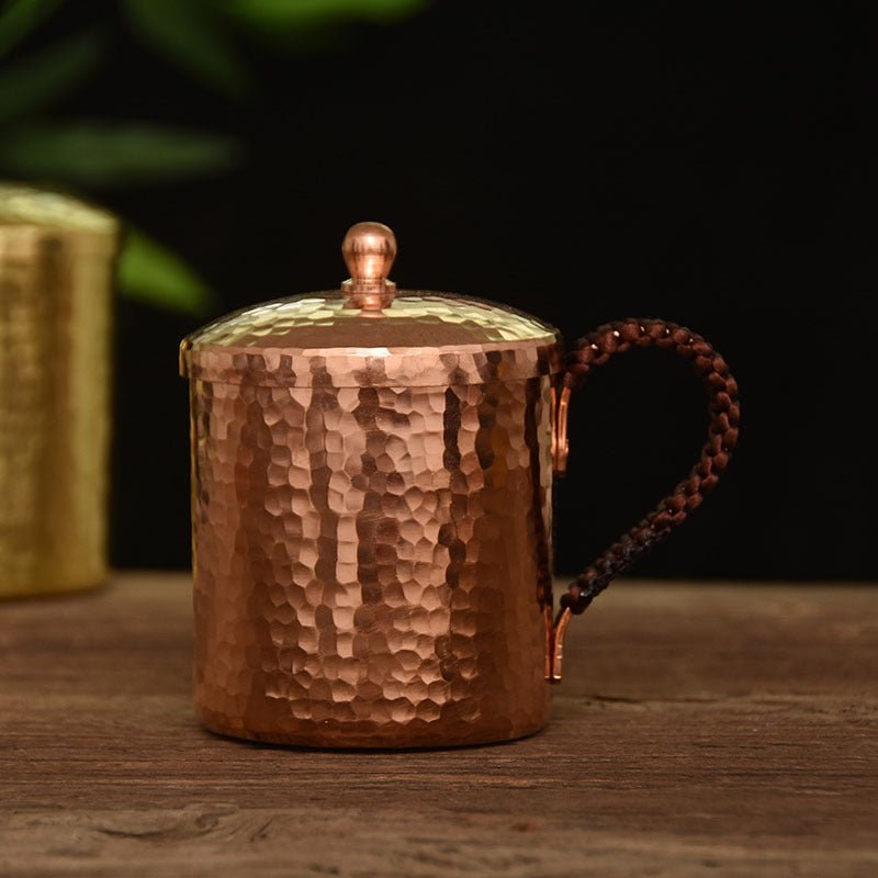 Hammered copper mug with braided handle and domed lid, front view on wooden surface