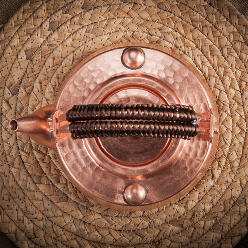 Top view of hammered copper teapot with cord-wrapped handle on a woven mat