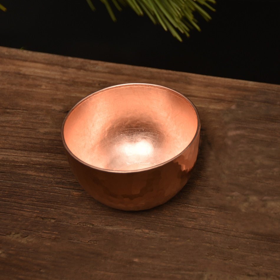 Hammered copper-tone cup without handle on wooden surface