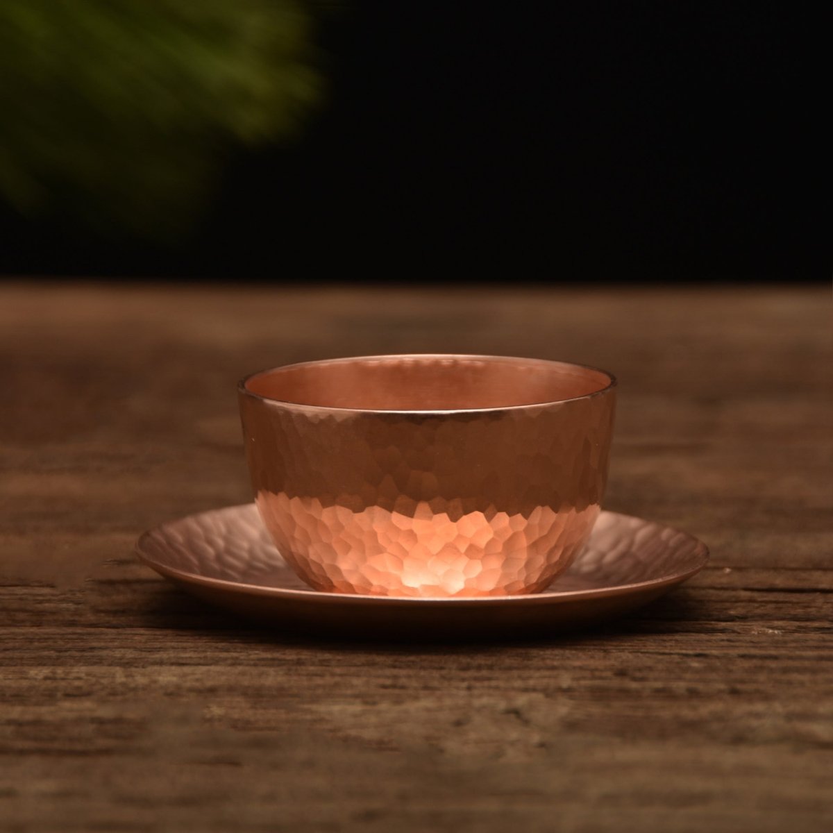 Hammered copper-tone teacup with saucer, bottom half textured, on wooden surface