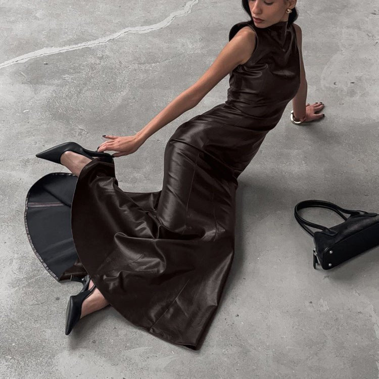 Model sitting on a concrete floor in the shiny brown dress, hem spread out, black bag beside her