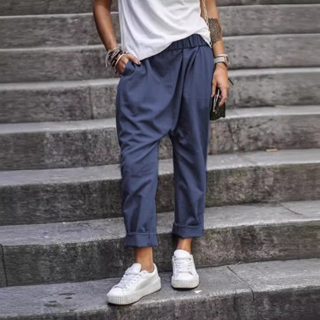 High-waist elastic harem trousers in dark blue, worn by a model on stone steps, front view with rolled cuffs and side pockets
