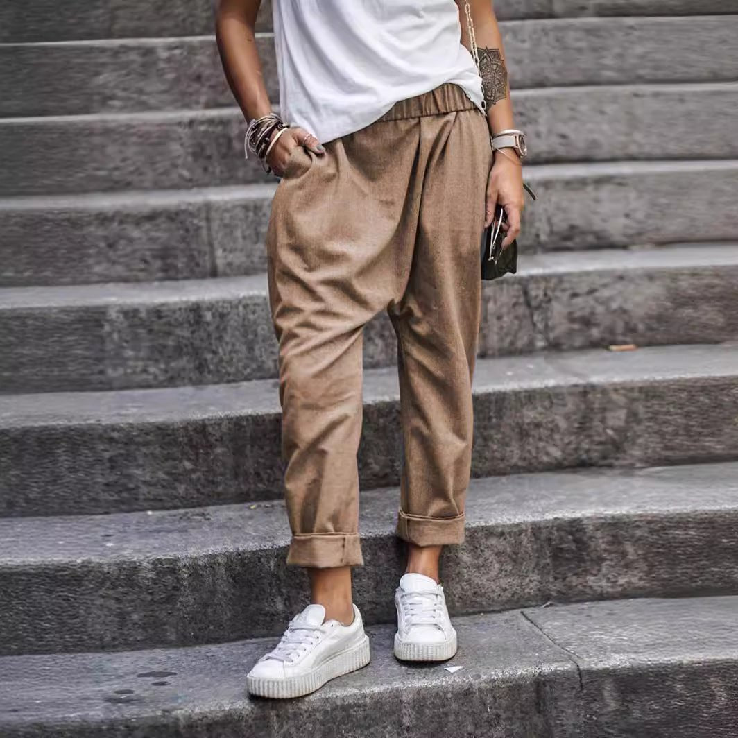 High-waist elastic harem trousers in beige, worn by a model on stone steps, front view with rolled cuffs and side pockets