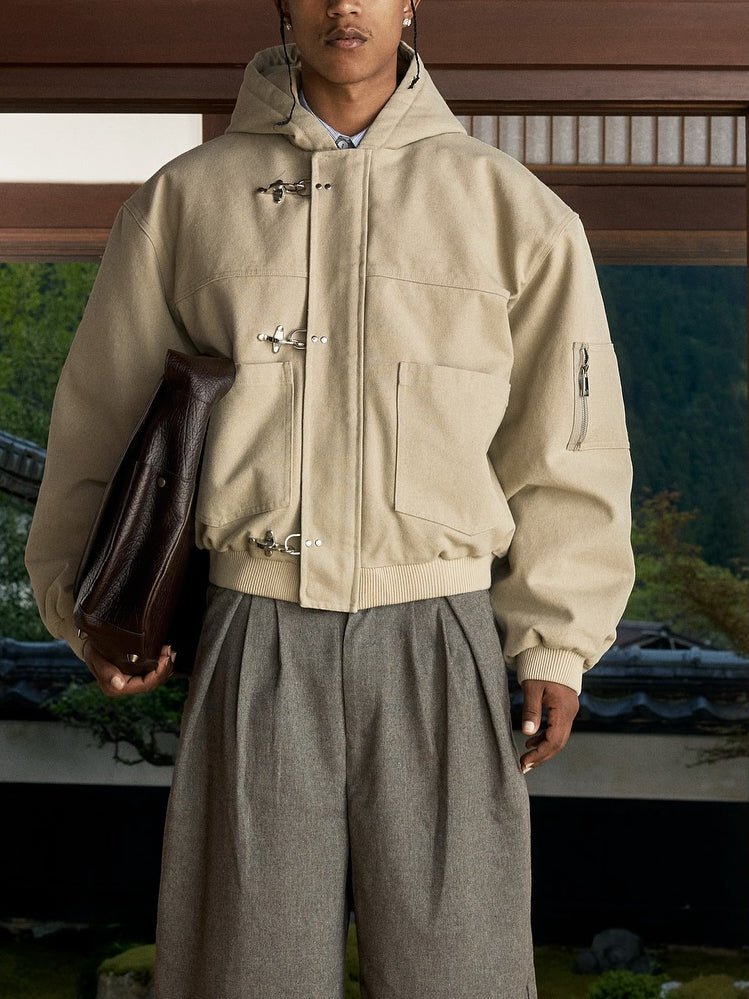 Short beige hooded jacket with hook clasps and patch pockets, worn with grey pleated trousers