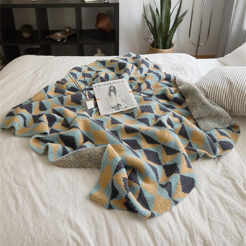Knit throw blanket with diamond pattern in blue, mustard and charcoal, spread loosely on a white bed