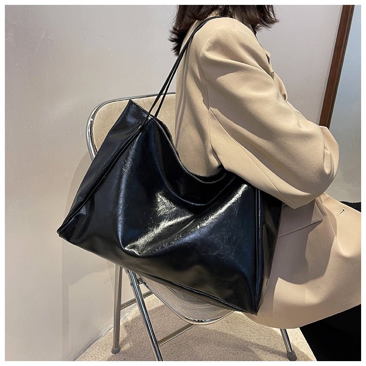 Black glossy tote bag on the shoulder of a seated person in a beige blazer