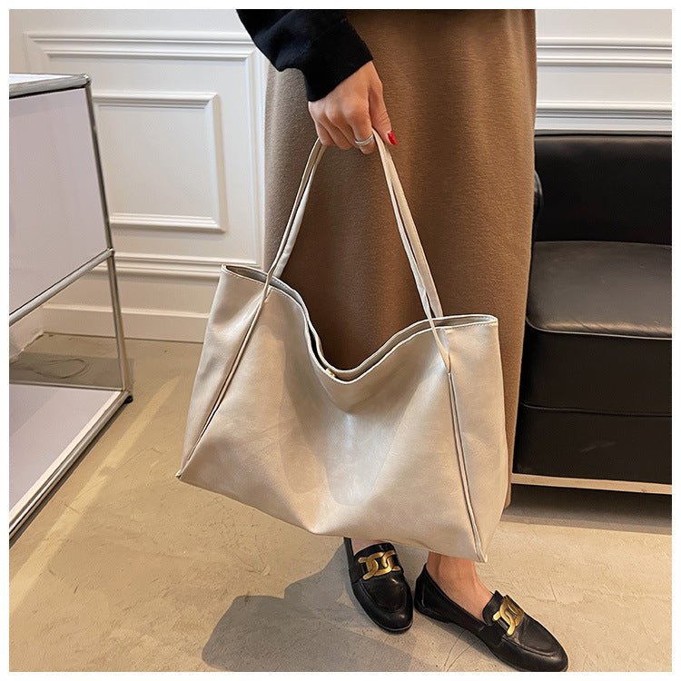 Off-white tote bag with a glossy finish held in one hand, seen from the front