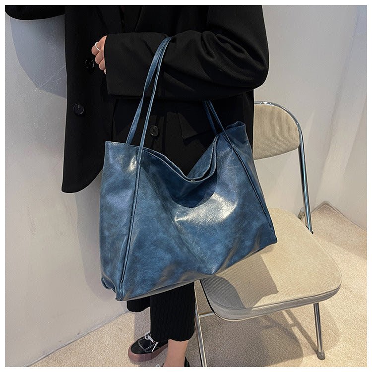 Blue glossy faux leather tote bag carried over the forearm by a person in a black blazer