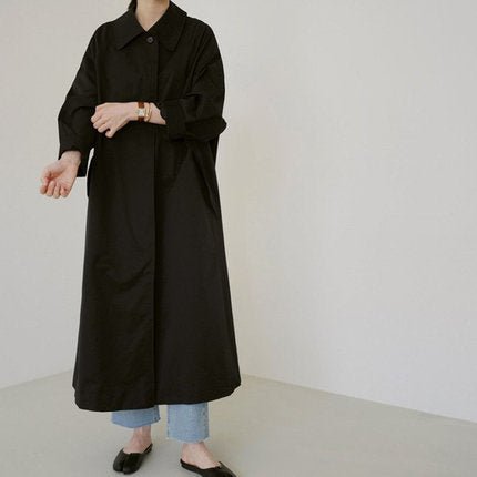 Black long button-front trench coat with flap pockets, front view on model, plain white background