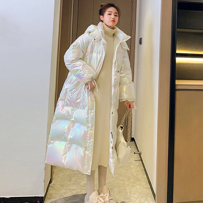 Woman in the long puffer coat in iridescent white, worn open over a cream knitted dress