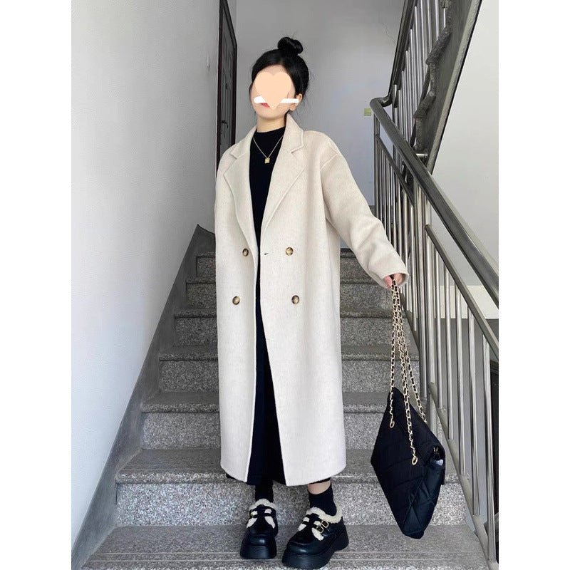 Long oversized double-breasted coat in oat white, worn by a model on stairs, front view holding a chain bag