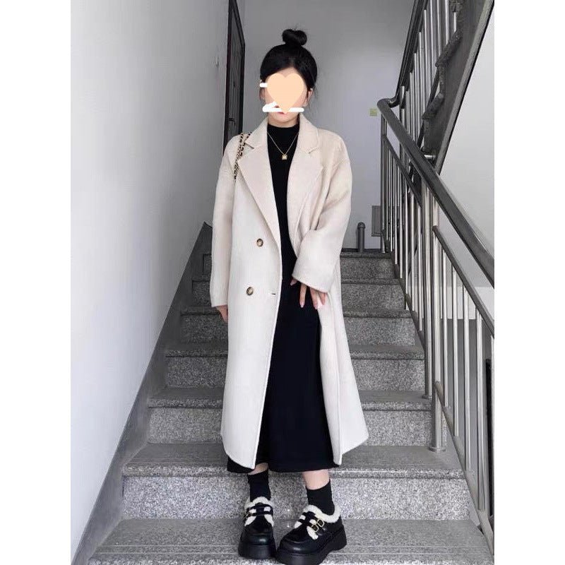 Long oversized double-breasted coat in oat white, worn by a model on stairs, front view with black outfit