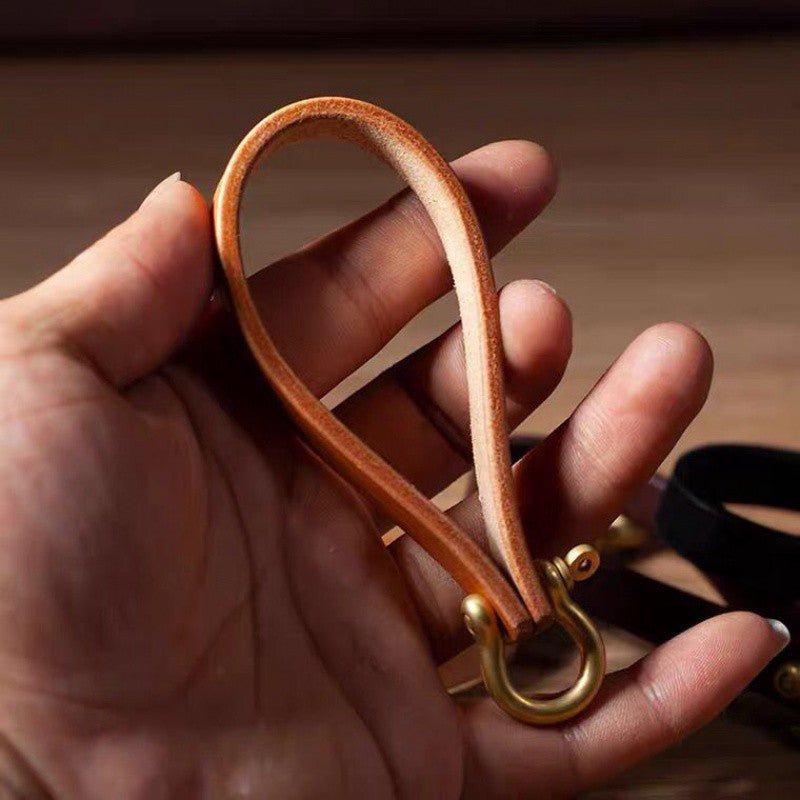 Hand holding a tan loop keychain with a brass-tone horseshoe clasp