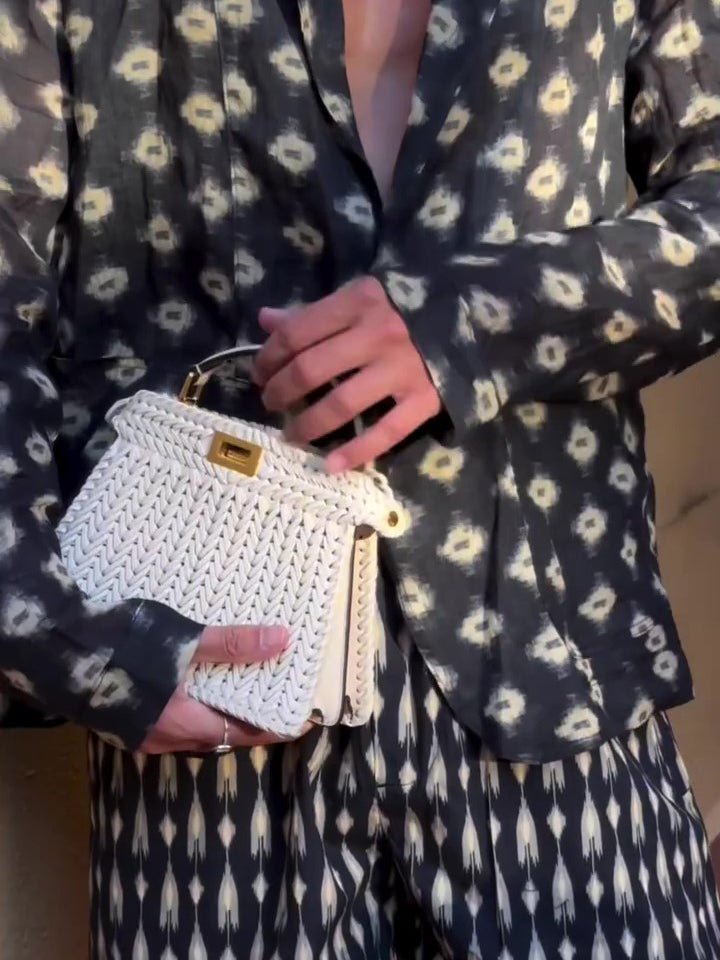 Close-up of the navy shirt-jacket with cream motifs over denser printed shorts; the cream bag is a prop
